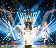 Een persoon houdt triomfantelijk een trofee omhoog op het podium, te midden van schitterende lichten en vallende confetti, wat een gevoel van succes en feestelijkheid uitstraalt