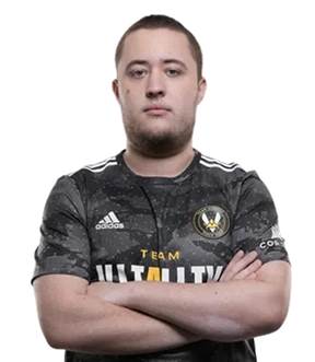 Een persoon met kort haar staat zelfverzekerd met de armen over elkaar, gekleed in een shirt van Team Vitality. De achtergrond is effen lichtgrijs