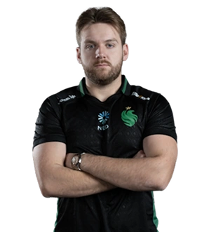 Een man in een zwart sportshirt met groene accenten staat zelfverzekerd met zijn armen over elkaar voor een zwarte achtergrond. Hij kijkt ernstig en geconcentreerd