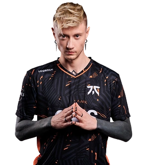 Een persoon met blond haar dat omhoog is gestyled staat zelfverzekerd, gekleed in een zwart-oranje esports-shirt, met de handen gevouwen. De blik is geconcentreerd en intens